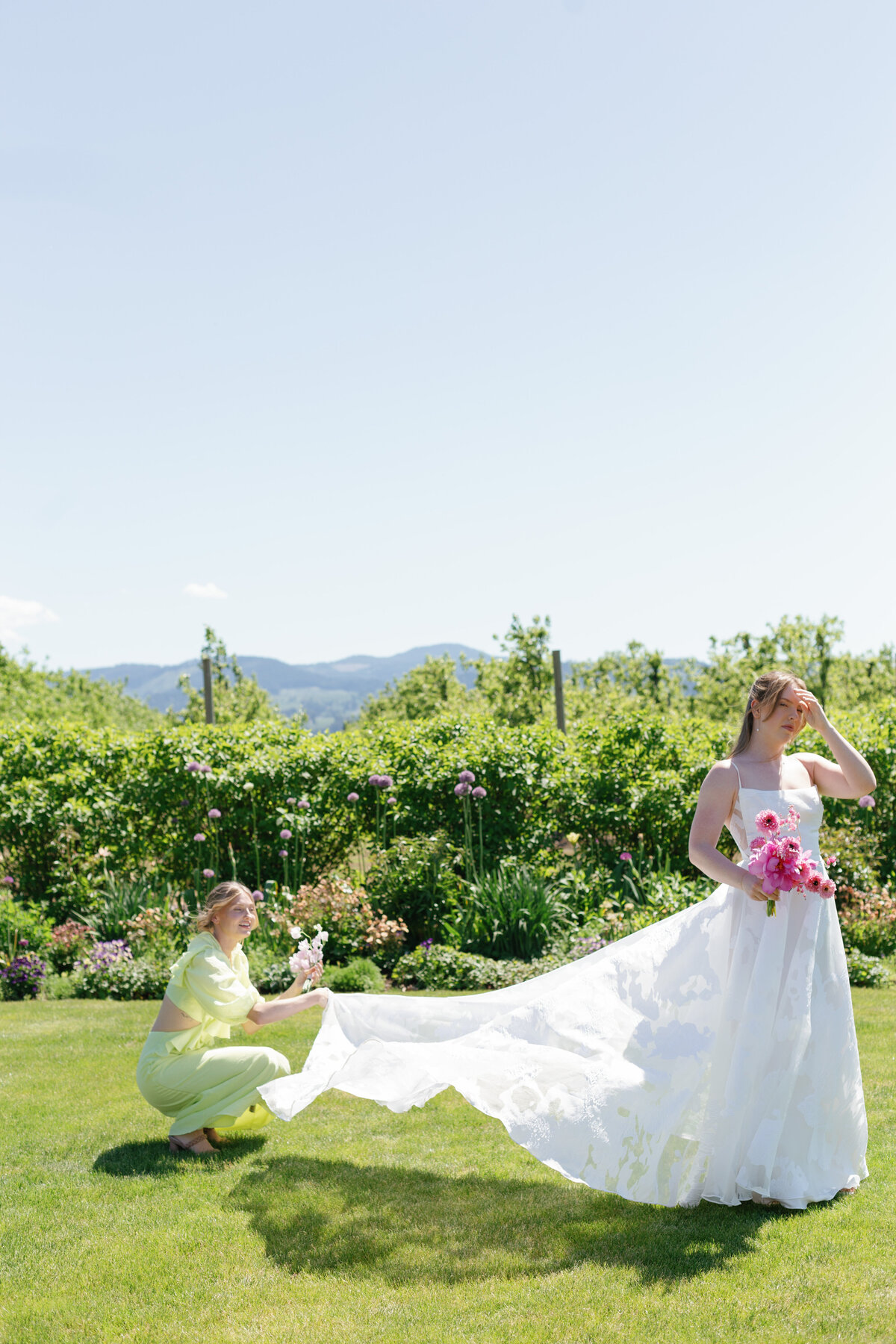 Bridesmaid fluffing brides dress in a field at The Orchard.