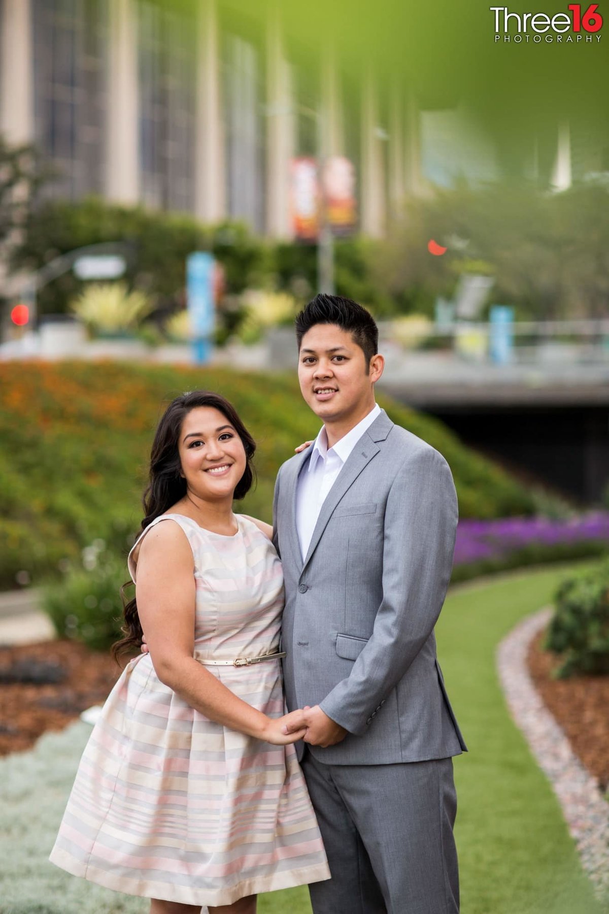 Engaged couple pose for photos while holding hands on the grass area at the Los Angeles Department of Water and Power Building