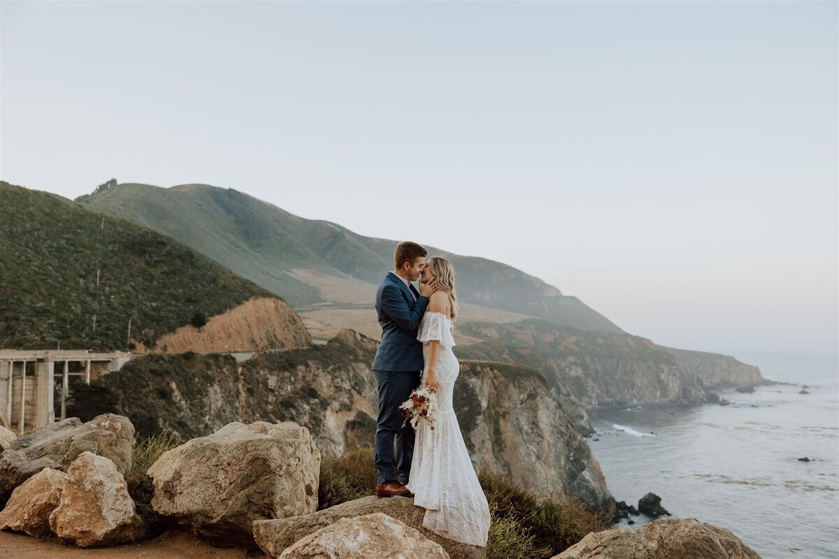 couple standing on rocks overlooking the ocean almost kissing