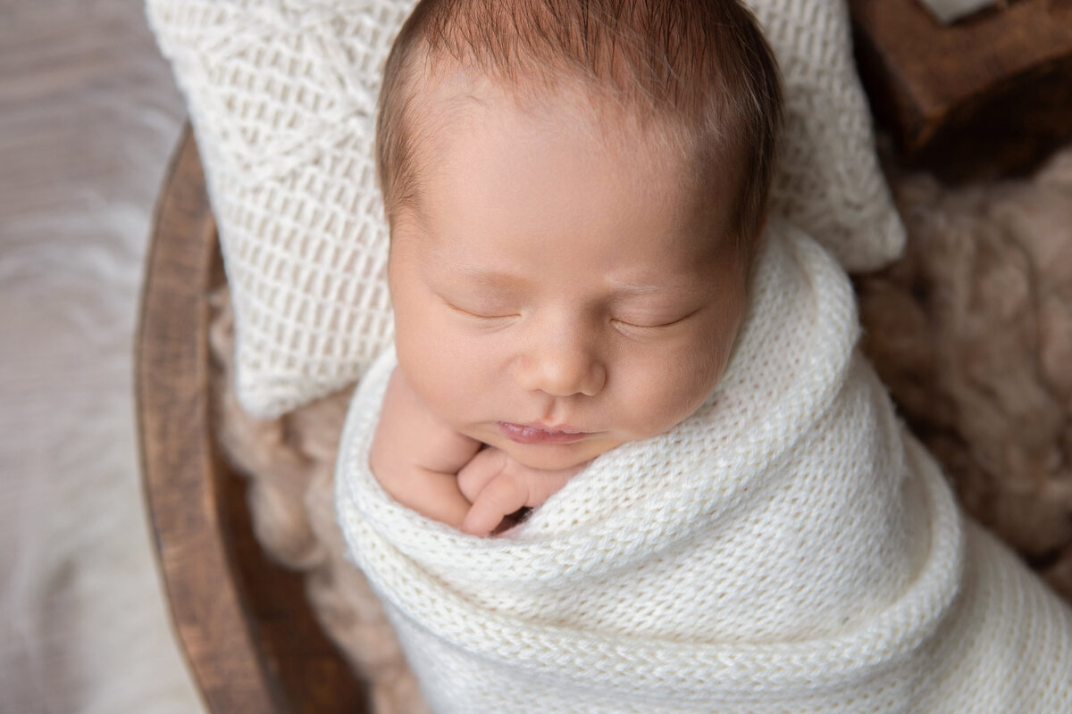 Newborn baby girl wrapped in white in a brown heart bowl newborn photography