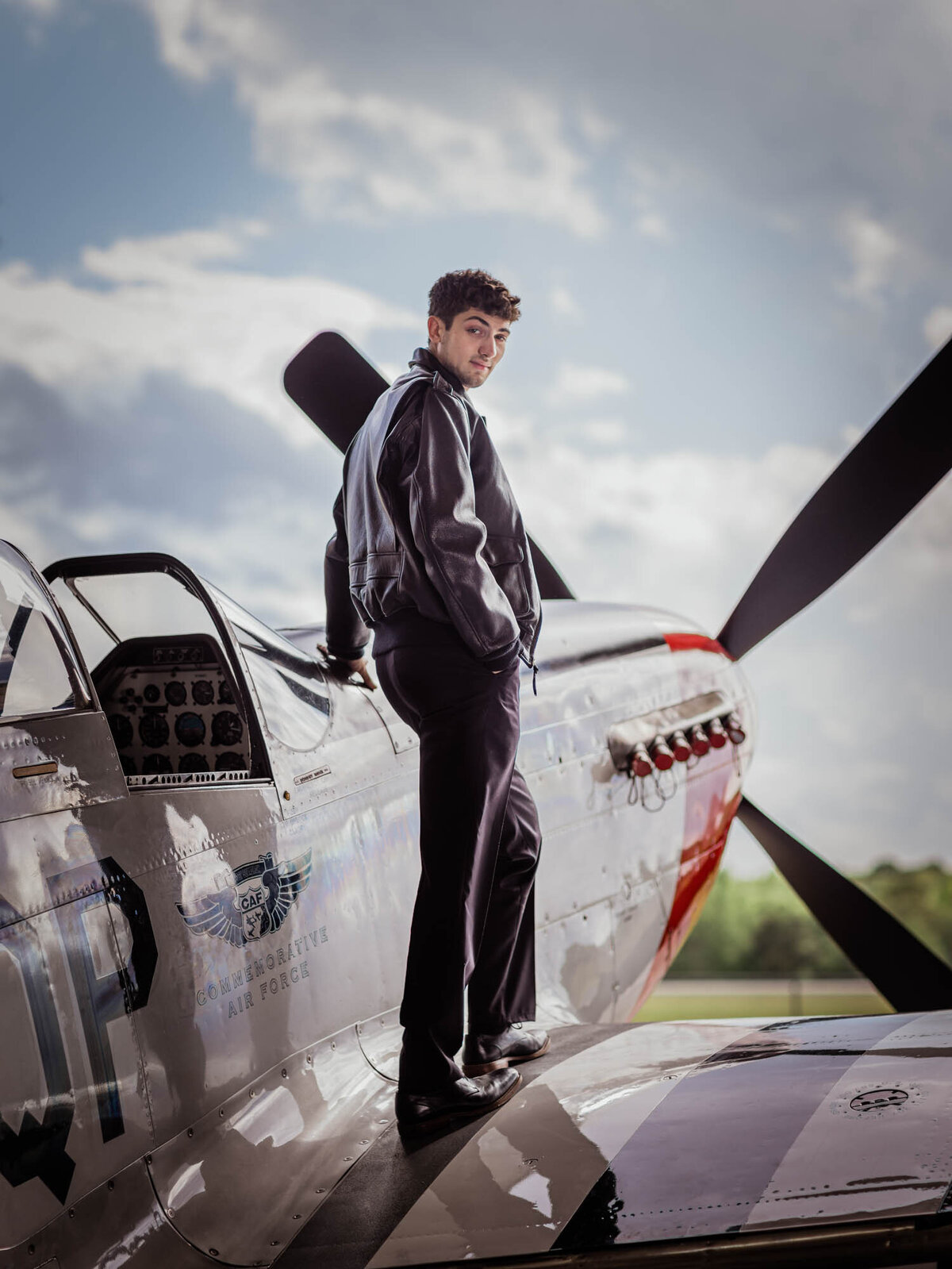 Senior portrait of a boy standing on the wind of a plane.