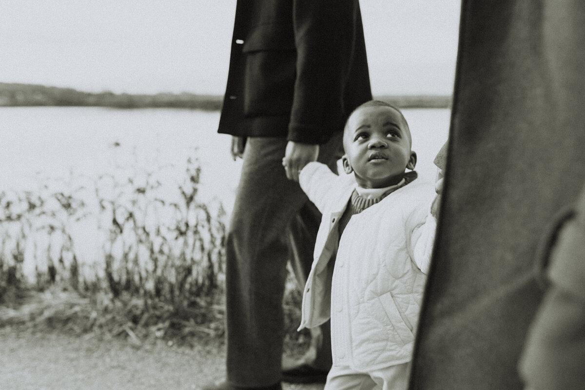 black and white photo of a little boy holding his mom and dads hands and looking up at his mom taken by a langley family photographer