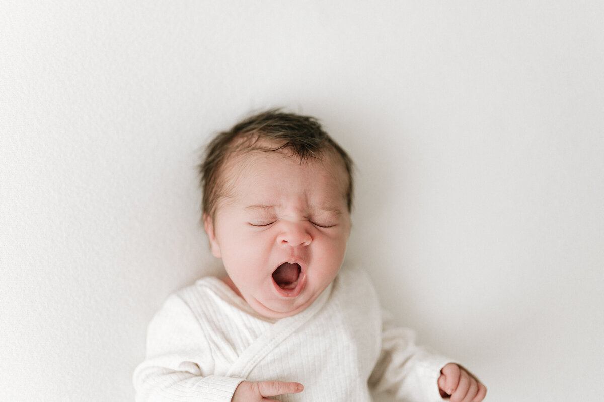 Newborn baby yawns for the camera during a photoshoot