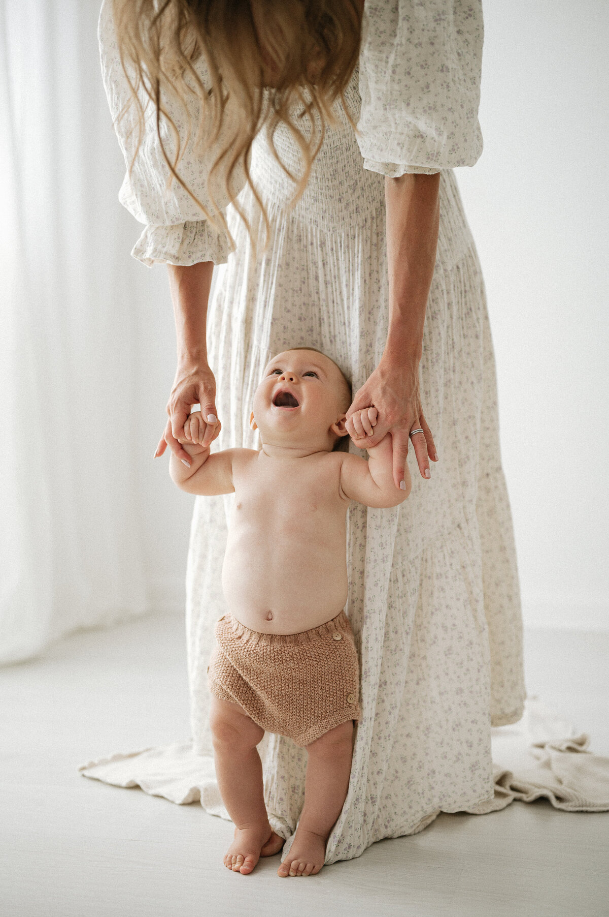 Studio photoshoot of a mother baby helping her baby stand