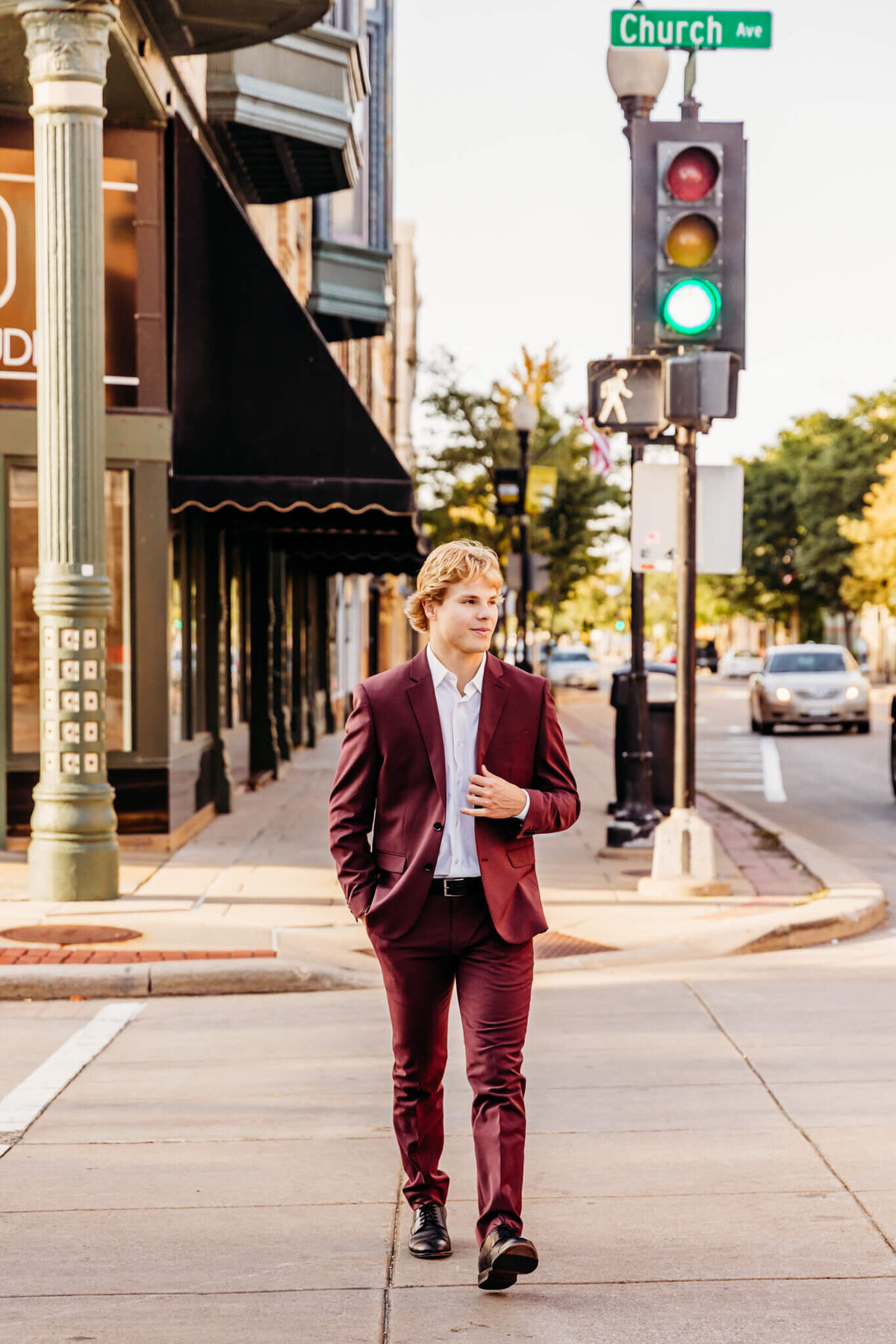 high school senior boy crossing the street and holding his suit jacket as he looks into traffic for senior pictures.