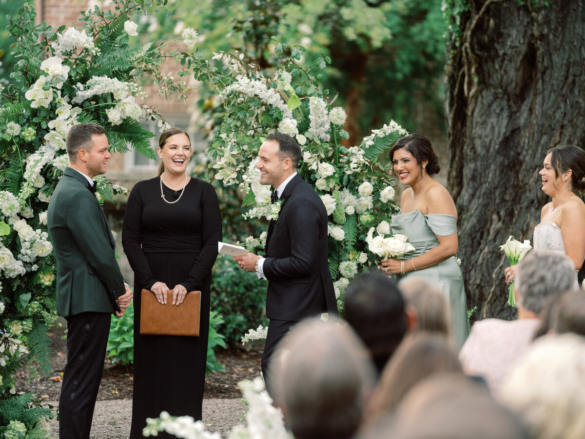 This image captures a beautiful wedding ceremony with a floral arch, a couple exchanging vows, and joyful guests in a serene outdoor setting, showcasing love and celebration.