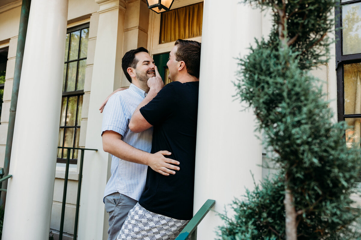 One groom sweetly pokes the other’s nose during a playful moment in front of white columns at Disney’s Boardwalk Inn resort.