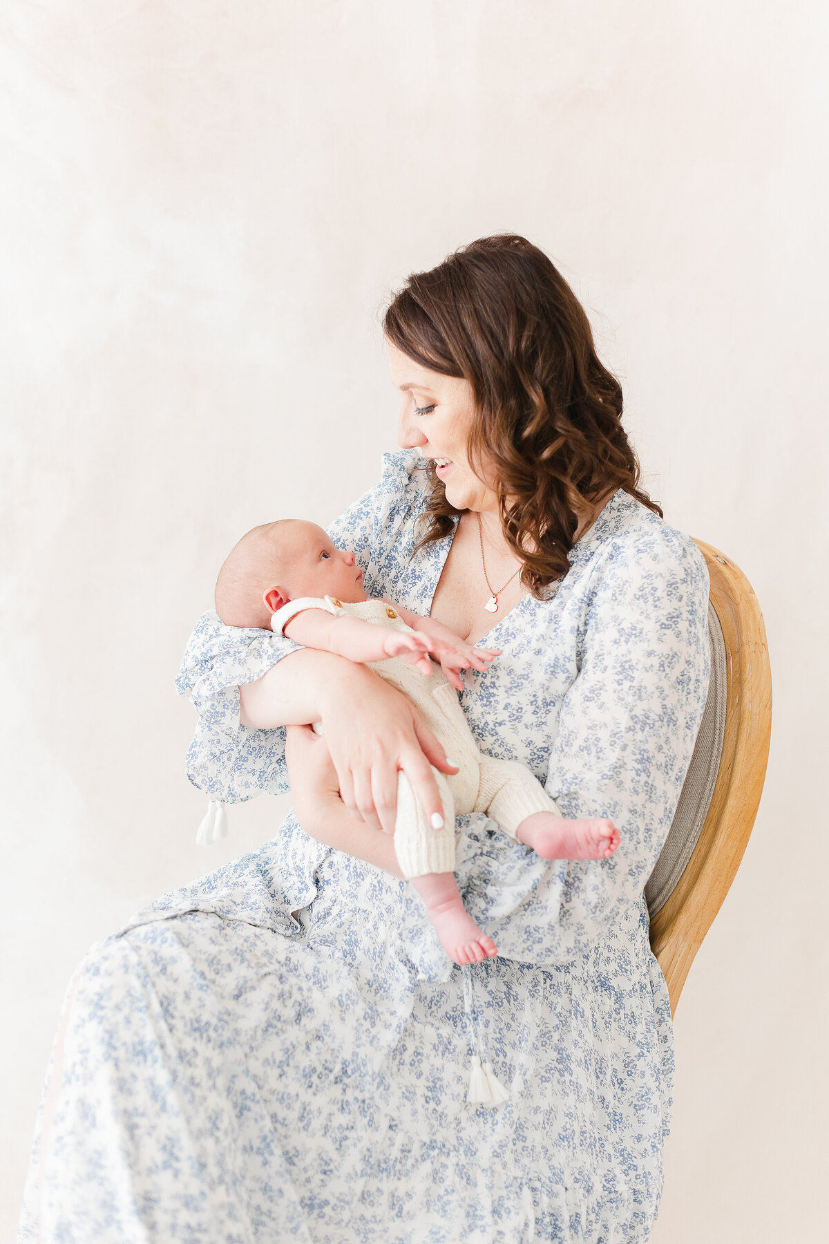 A Nova Studio Photography photo of a mother sitting down in a chair looking down at her infant in her lap
