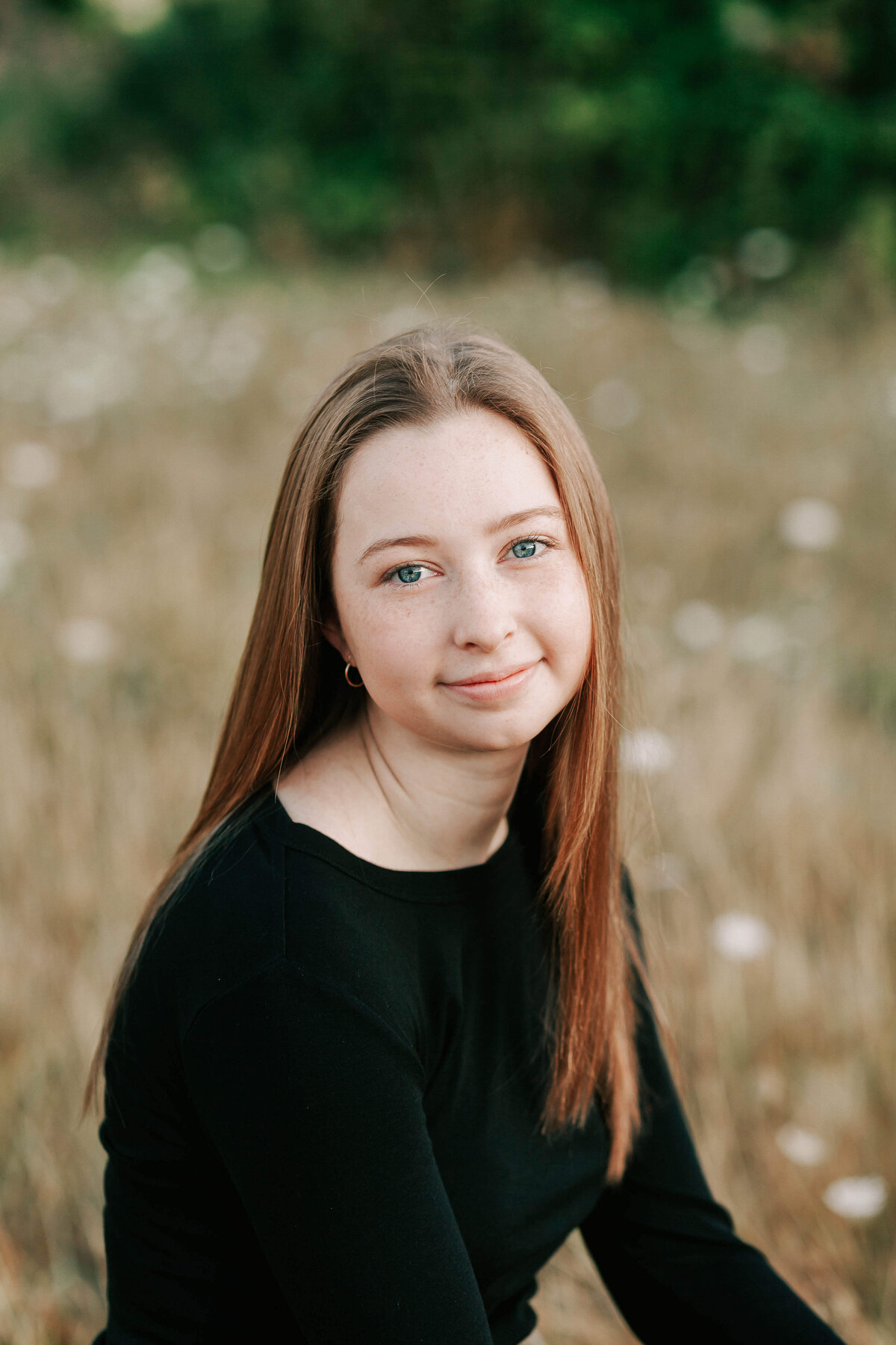 A girl with long hair sits in a field with white flowers