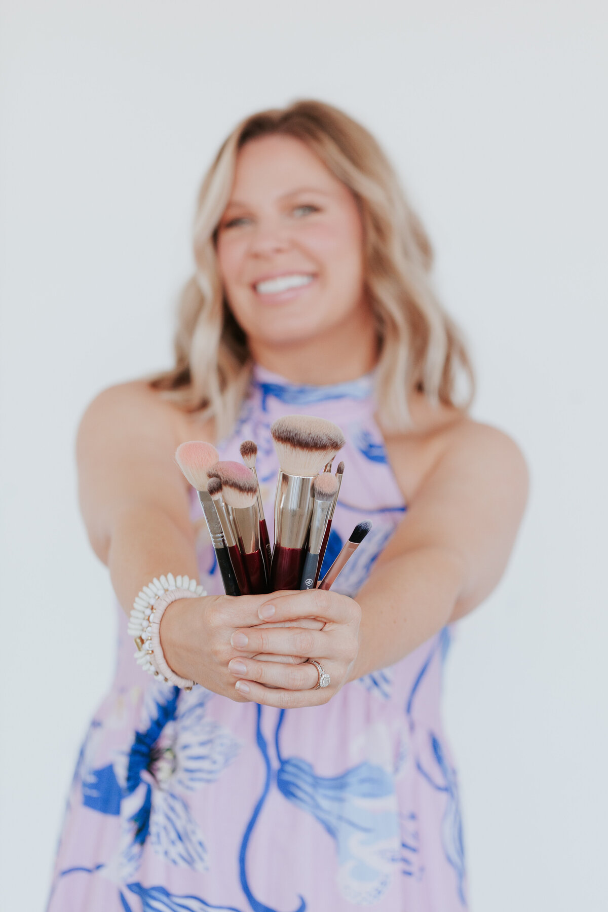 playful-photo-makeup-artist-holding-makeup-brushes-toward-camera-for-brand-session-the-frame-charlotte