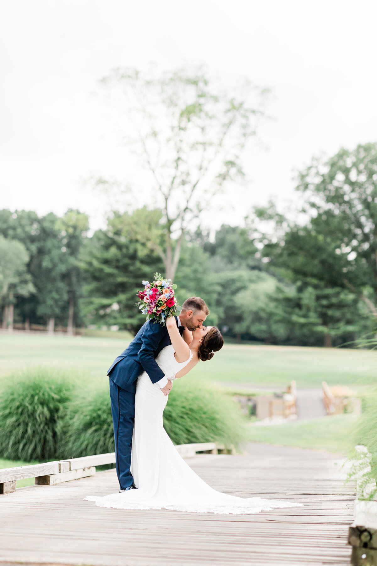 Couple facing each other in a dip, bride has colorful bouquet and arms around groom kissing