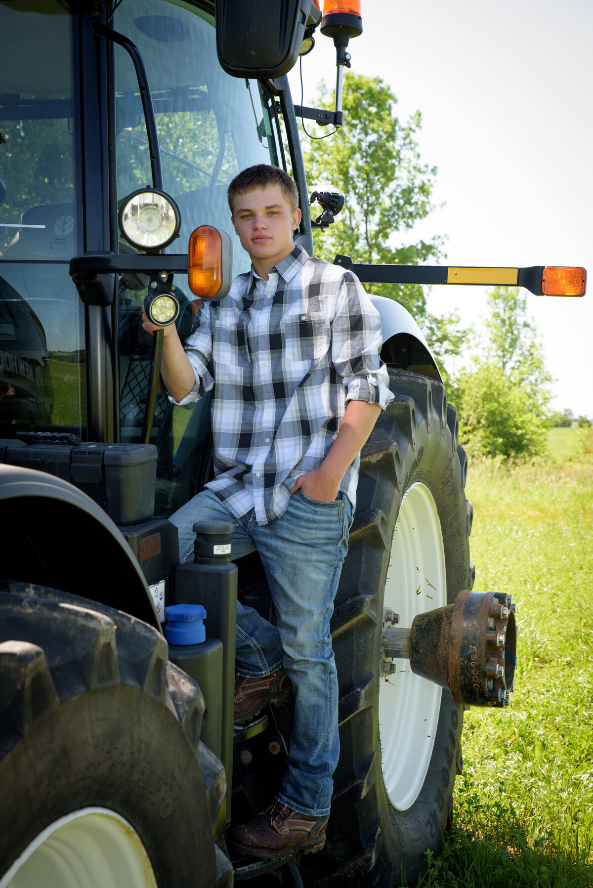 Luxemburg Casco high school senior boy wearing a black and white plaid button down shirt and jeans by a black New Holland tractor in farm field at his home near Green Bay, Wisconsin.