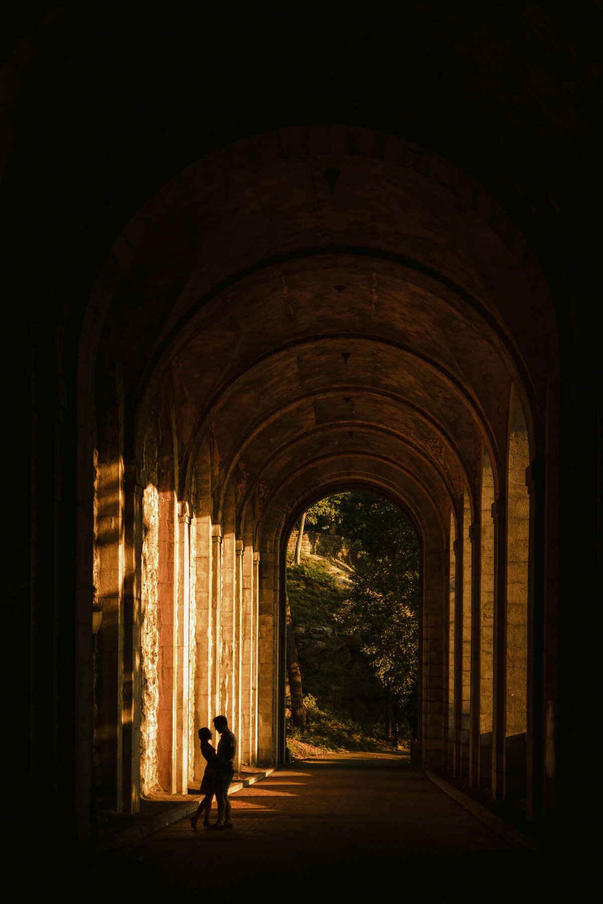 The silhouette of a couple standing together under a large arched walkway.