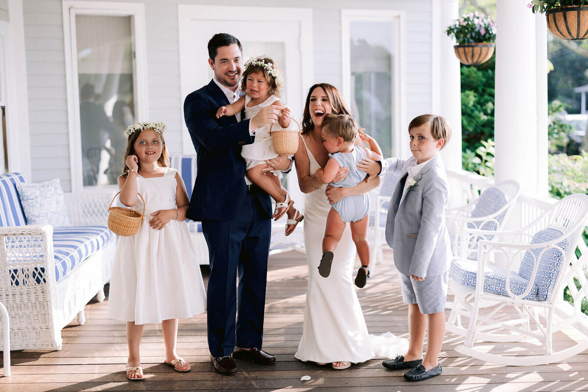 The bride and the groom are each carrying a baby, with two other children standing beside them in Cape Cod Summer Tent, MA.