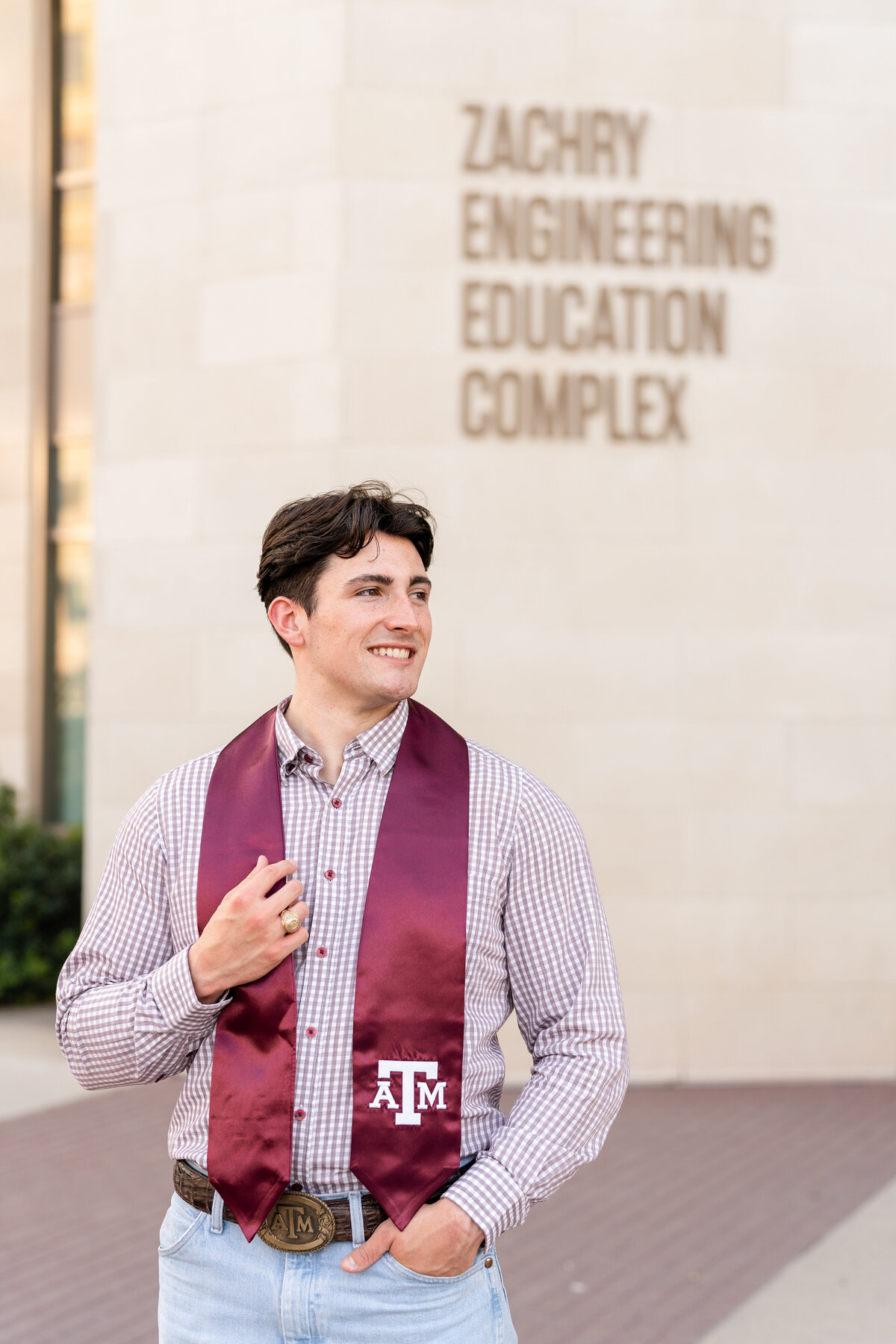 Texas A&M senior guy holding Aggie stole and smiling away while wearing jeans and button up in front of Zachry Engineering Complex