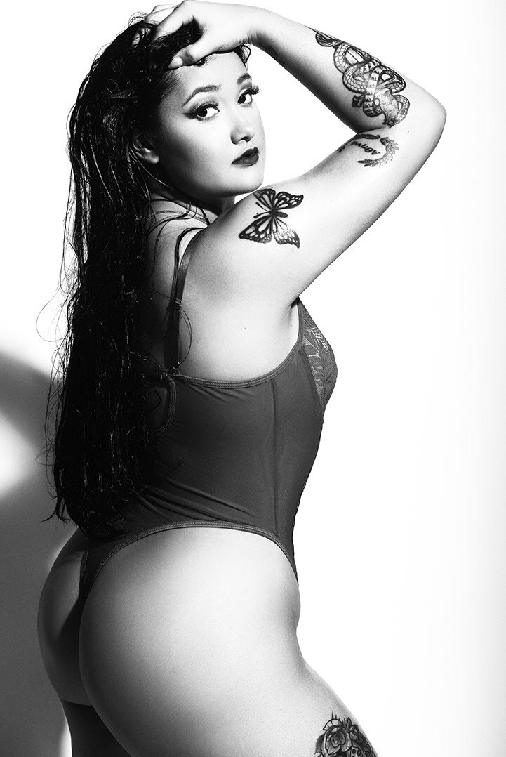 A Herb Ritts style black and white image of a woman in lingerie with wet hair and tatoos.