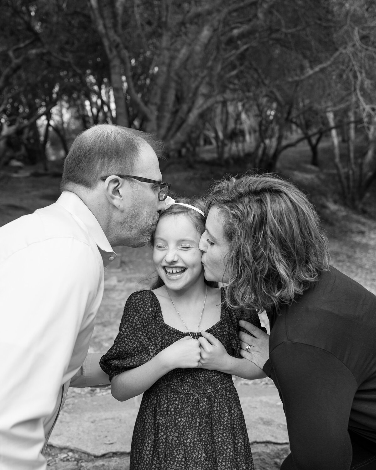 Parents give their daughter a kiss on her cheeks