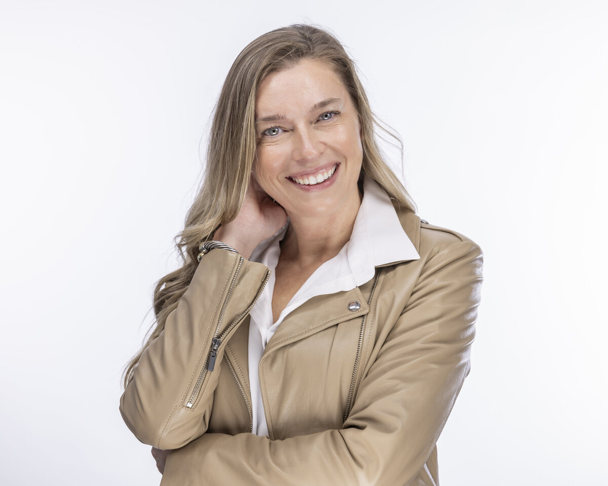 Headshot in MA of smiling woman with long hair in tan jacket, posed against white backdrop by Rob Faber Photography.
