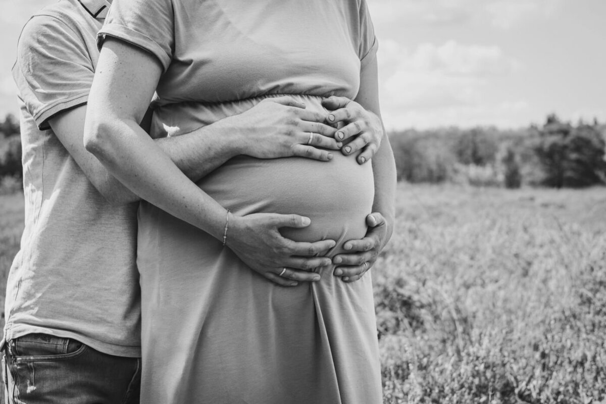 Een intiem zwart-wit zwangerschapsportret, met de nadruk op de handen van de ouders op de buik van de moeder.