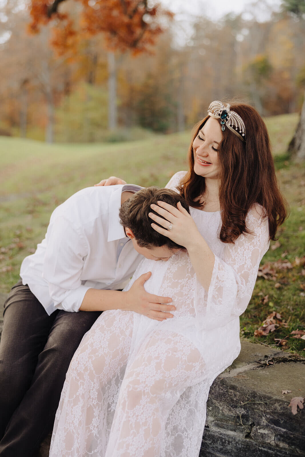 Couple sitting on wall kissing baby bump for maternity photo session in Fingerlakes, NY