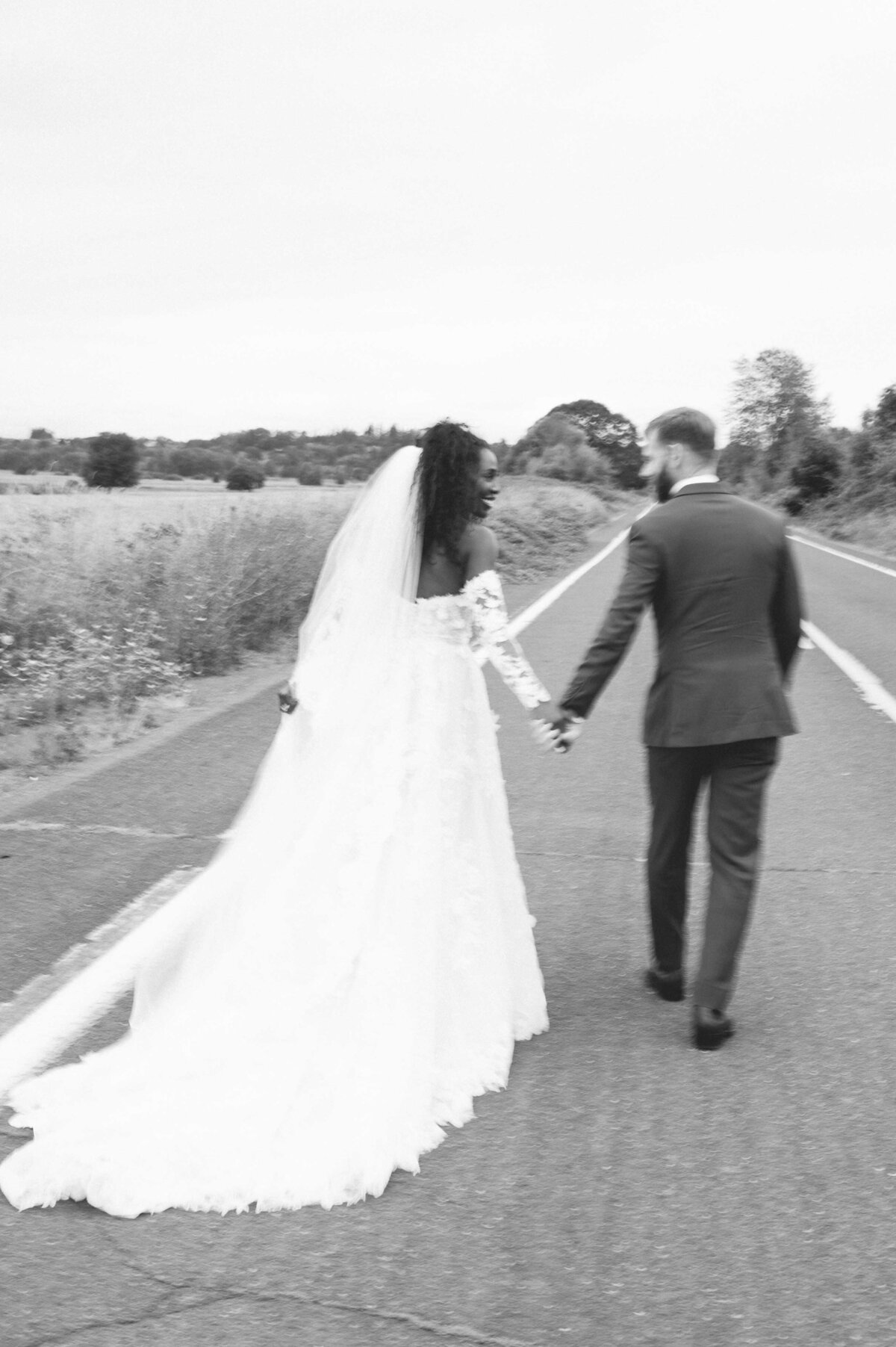 biracial bride and groom in editorial photo running along a road in black and white with motion blur