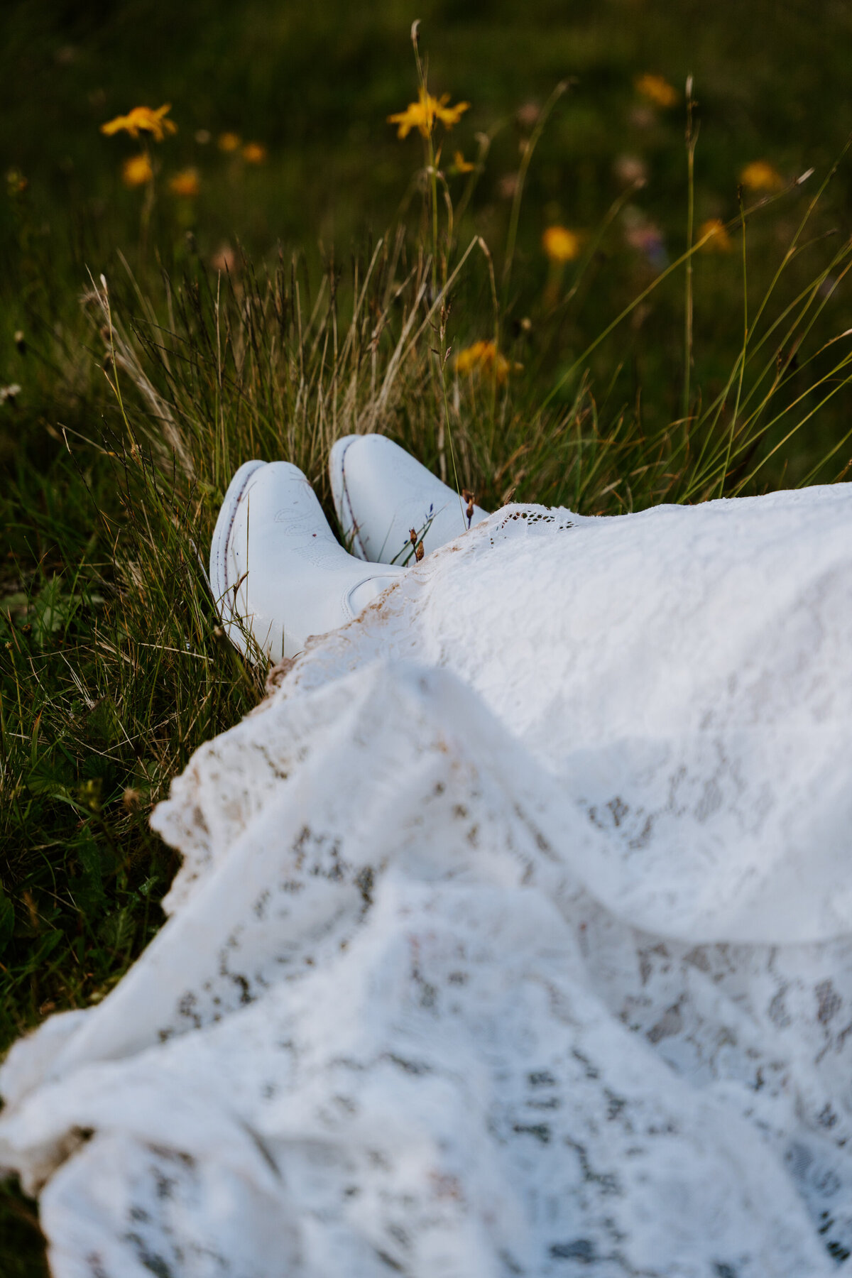 Bride’s white boots and lace dress in alpine grass