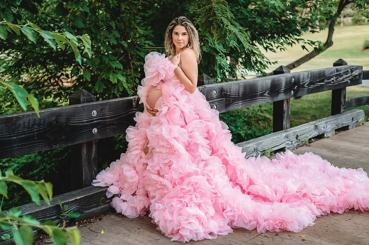 Stunning expectant mom posing on a bridge in a ruffle pink gown  at Battlefield Park.