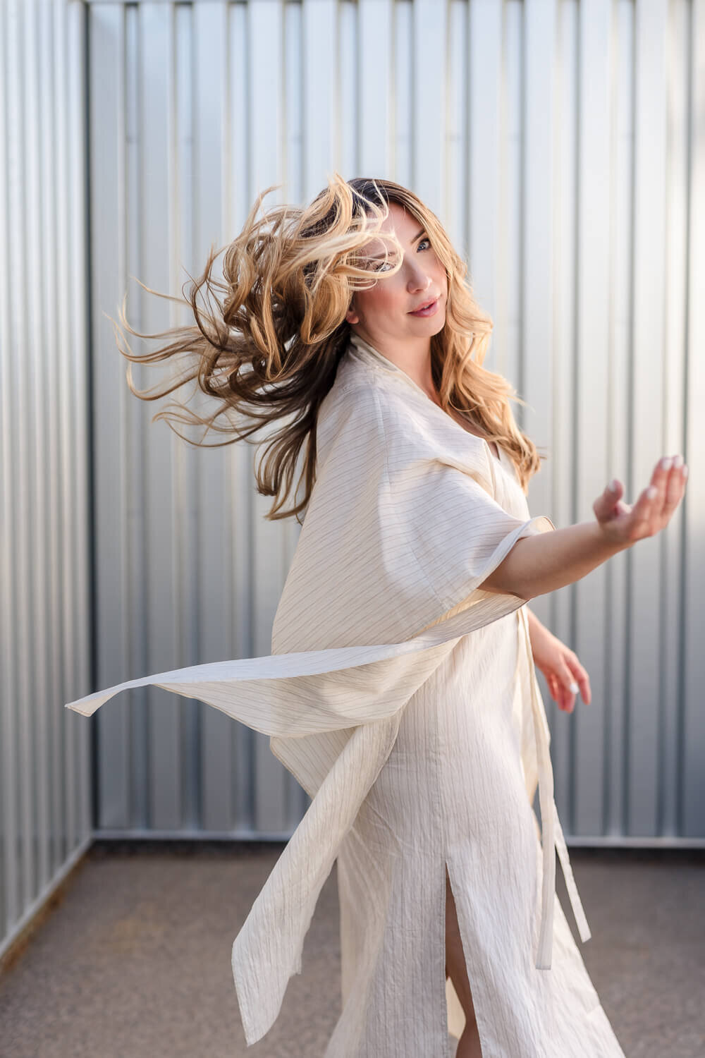Elegant woman in white dress mid spin with hair and dress flying against a metal backdrop