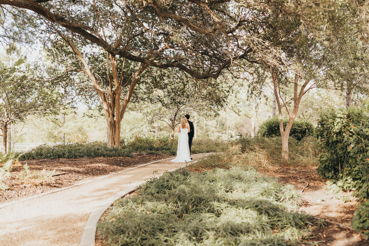 bride and groom have a quiet minute alone underneath large trees in Houston Park, along gravel pathway.