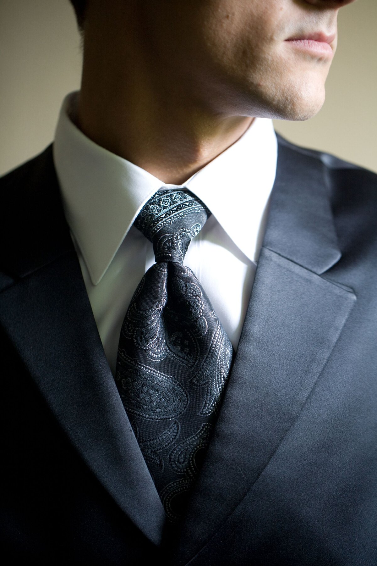 A close-up shot of the groom adjusting or wearing his tie, highlighting the details of his formal attire. This image focuses on the groom's refined style and the elegance of his outfit, capturing a moment of preparation and sophistication in his wedding portrait.