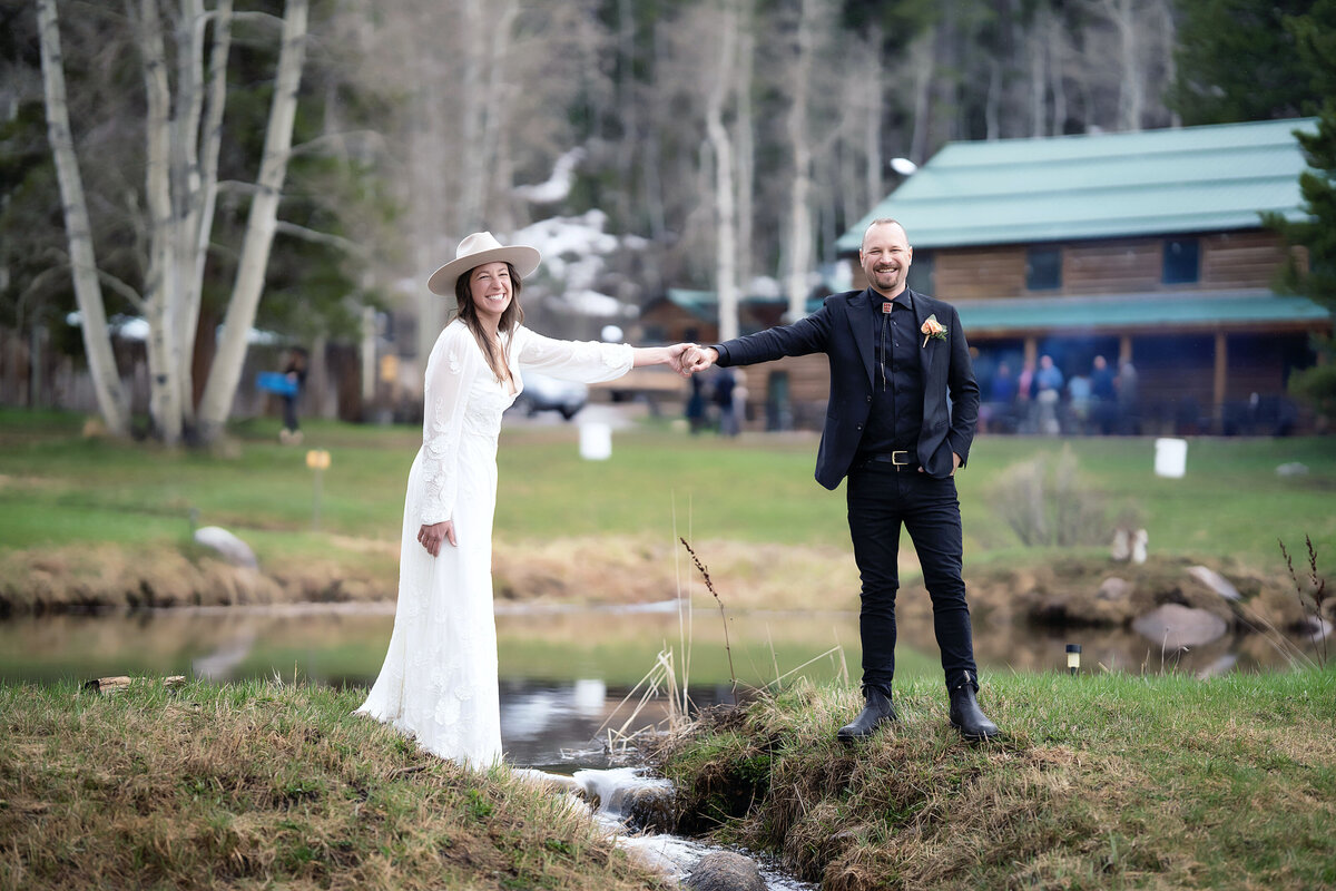 Bride and groom hold hands across a small creek on their wedding day, in Aspen Colorado,