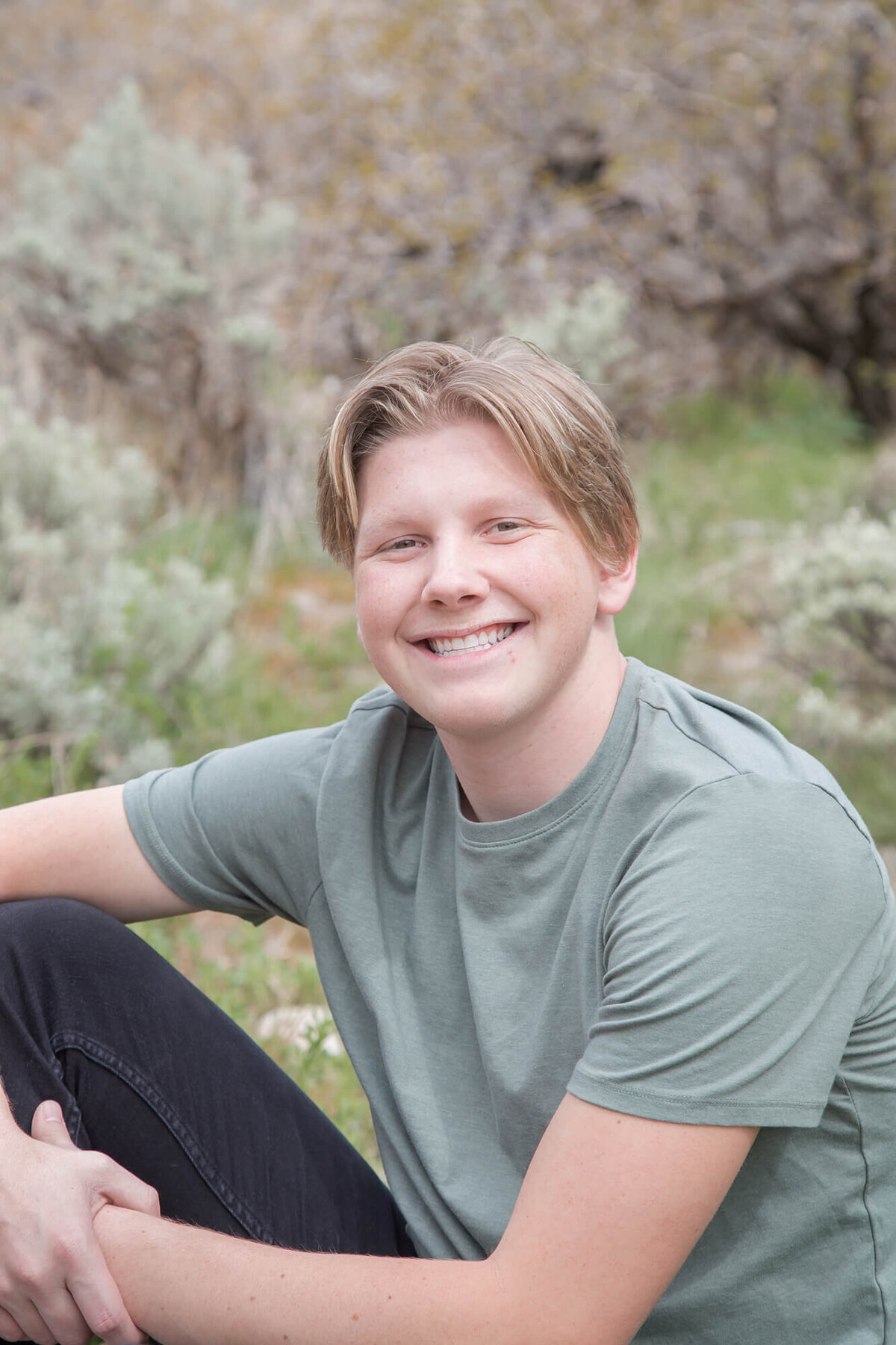 Senior boy smiling while sitting in sage brush at Rock Canyon Park