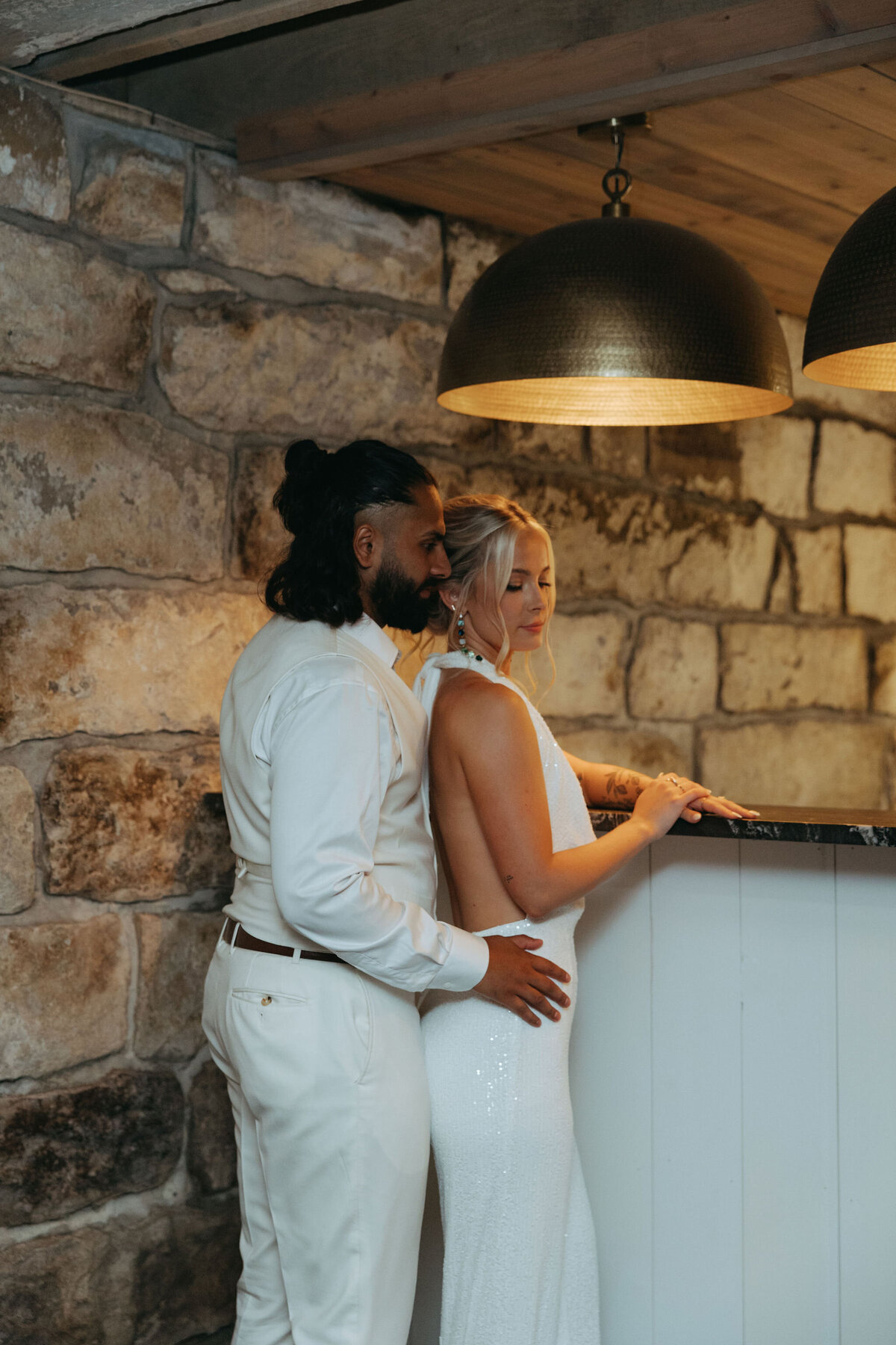 a bride and groom all dressed in white at the downstairs bar with hammered brass pendant lights at Willowbrook Wedding venue