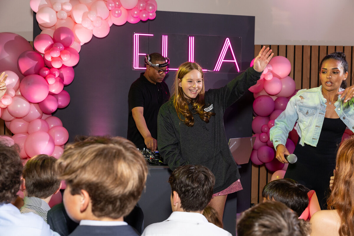 A girl on stage waving to people on a dance floor