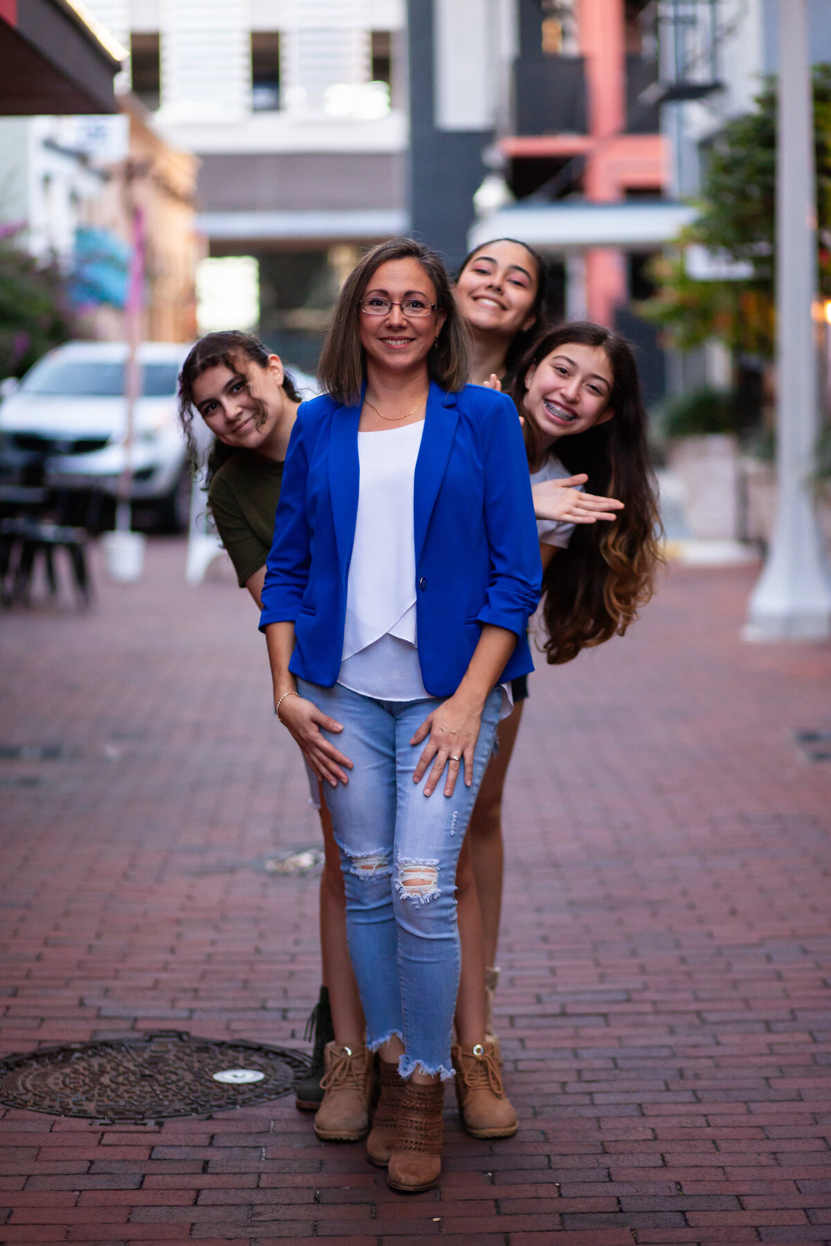 mom poses for the camera with her 3 daughters peeking out from behind her
