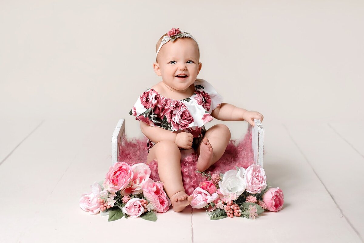 Baby girl in pink floral romper smiling during 1 year photo shoot.