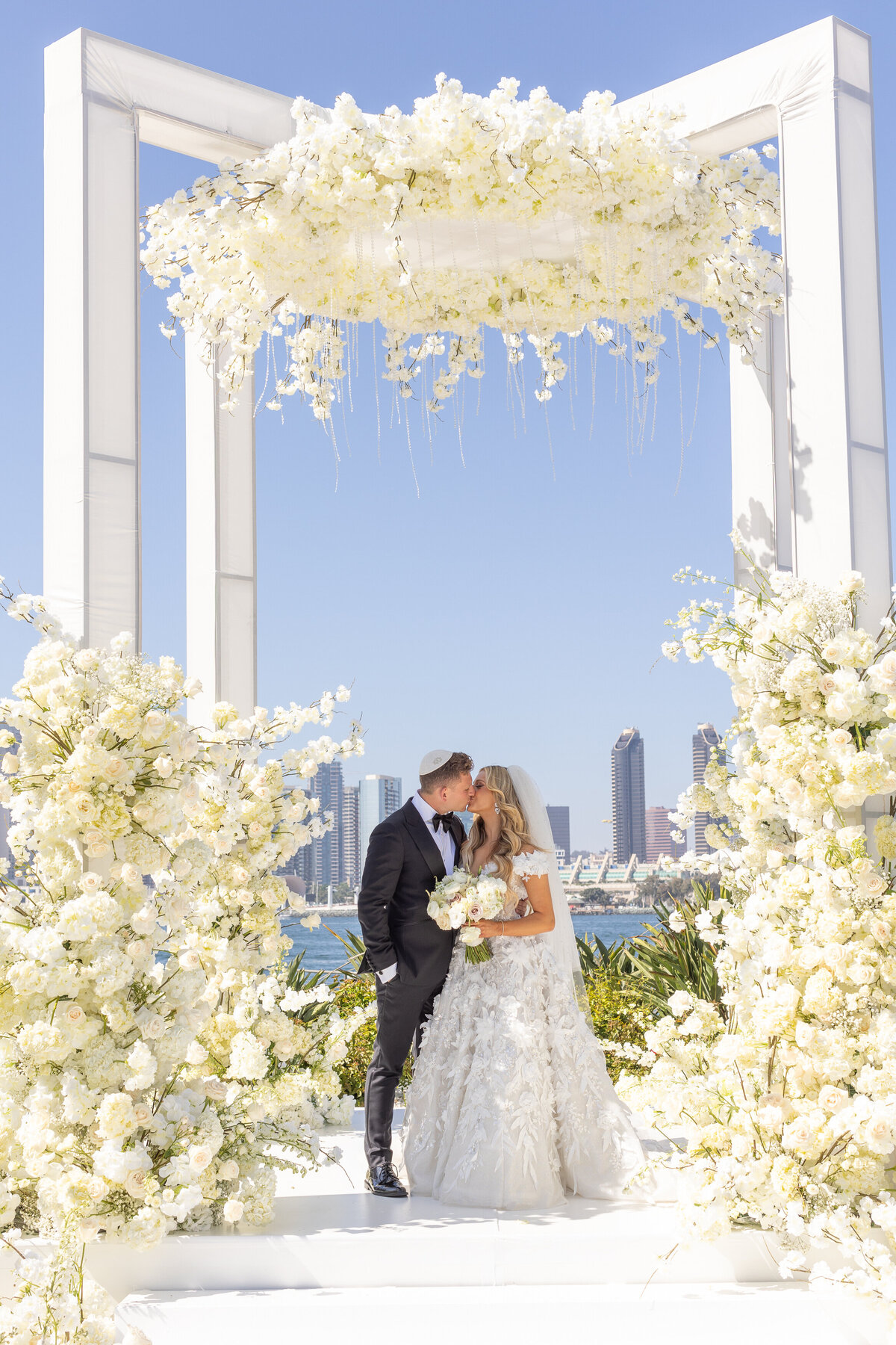 A bride and groom kissing under an extravagant flower arch