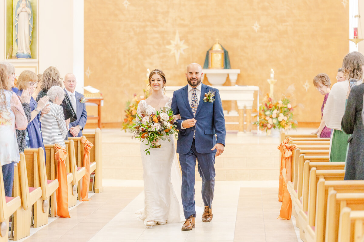 Newlyweds exit their church wedding ceremony while walking up the aisle to cheers