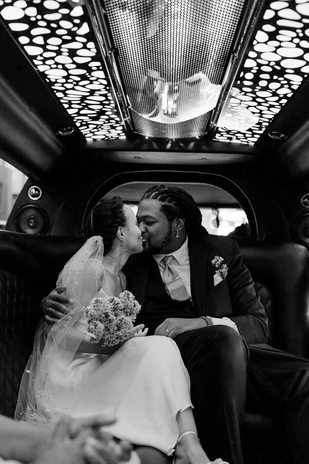 black and white photo of a bride and a groom kissing in the back of a limo