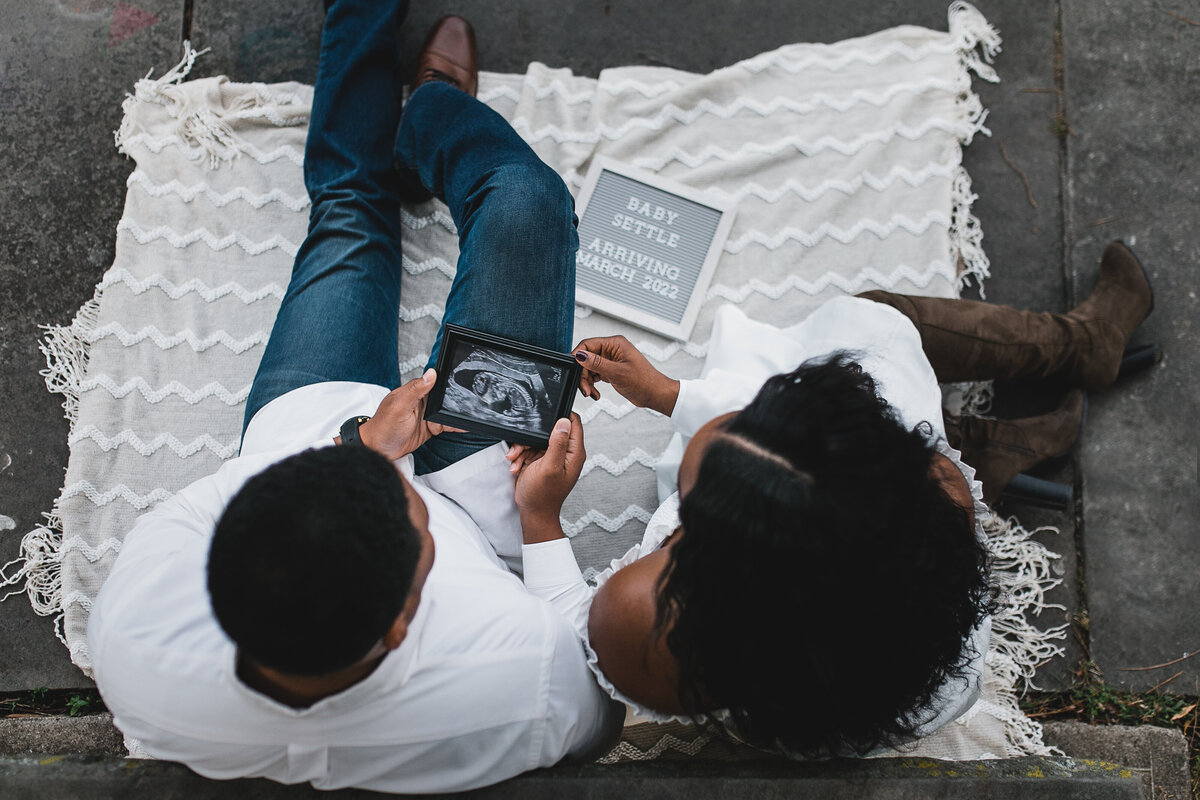 Maternity photograph of a woman and man sitting  on a couch looking at ultrasound picture.