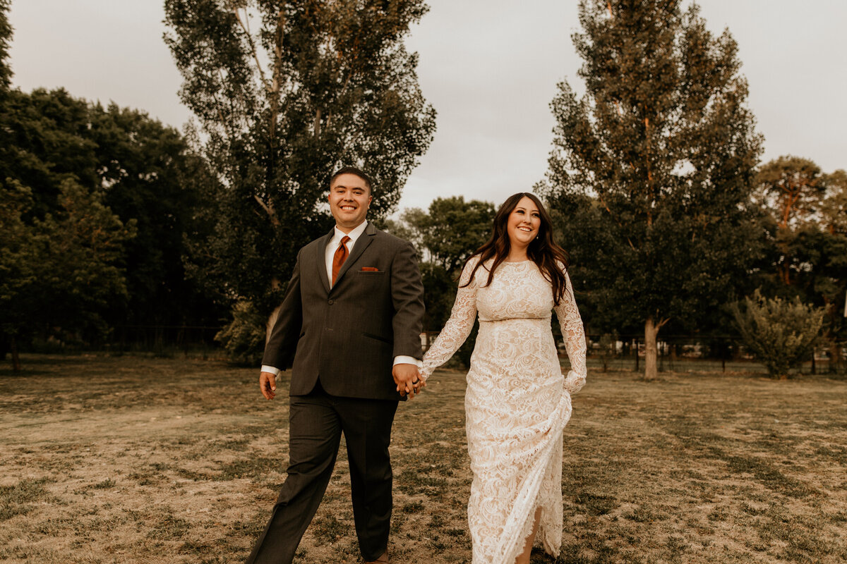 bride and groom walking through a field together on their New Mexico property