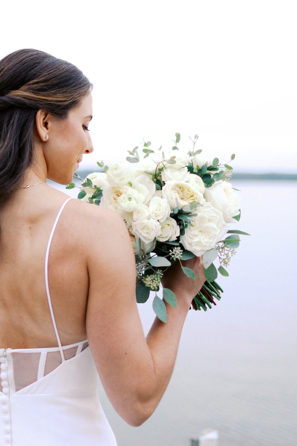 Bride holding her gorgeous bouquet of white roses, admiring its beauty on her wedding day — captured by Minnesota wedding photographer.