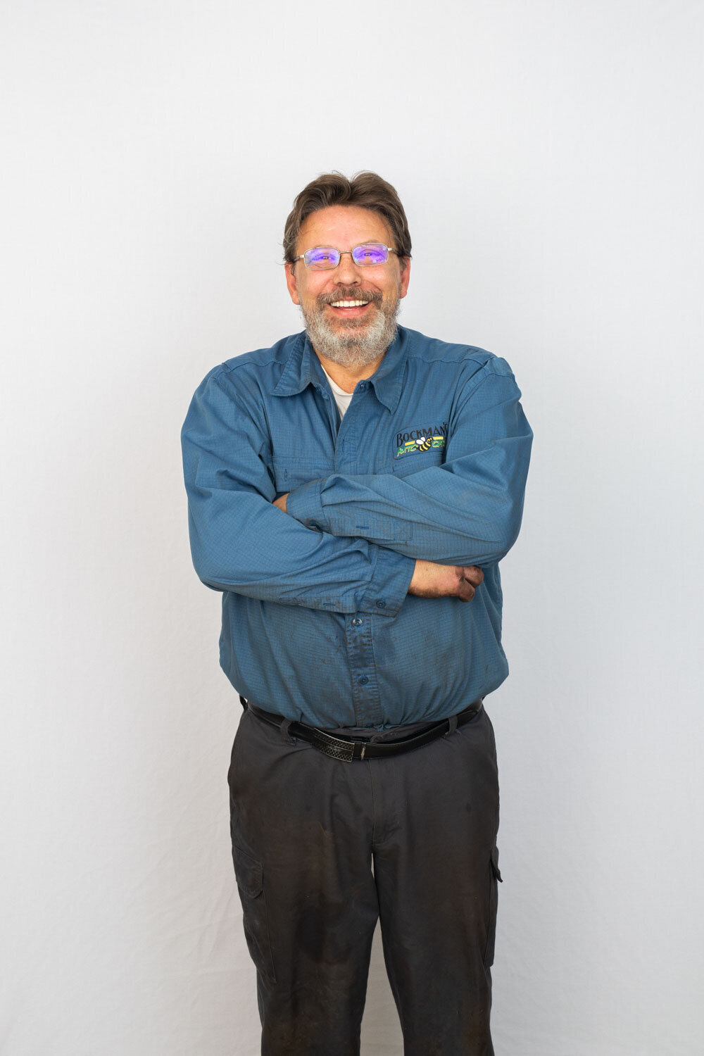 A man wearing glasses and a blue shirt is standing with his arms crossed