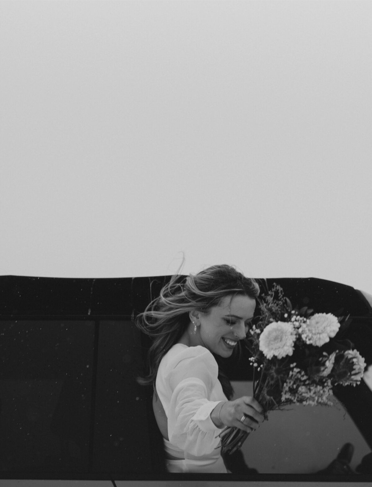 bride holds her bouquet of flowers as she hangs out the jeep bronco window and the wind blows her hair