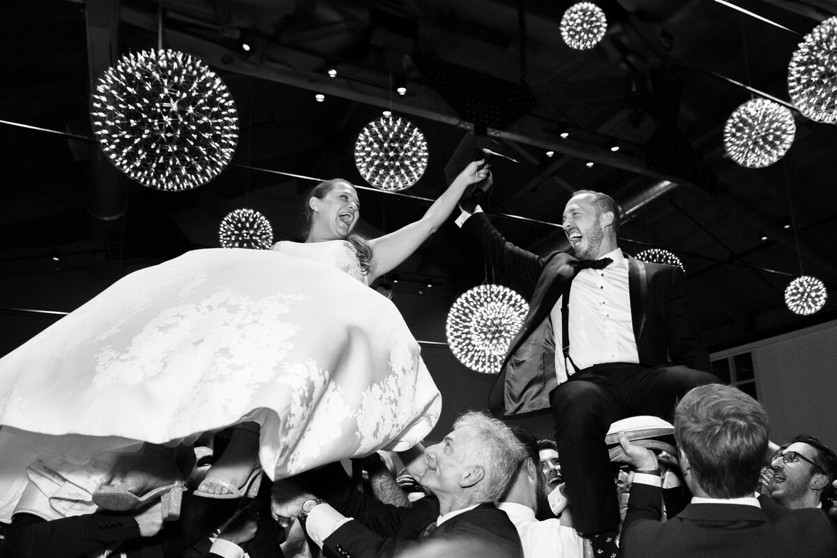 Black and white photo of a wedding couple behind held up by their wedding guests.