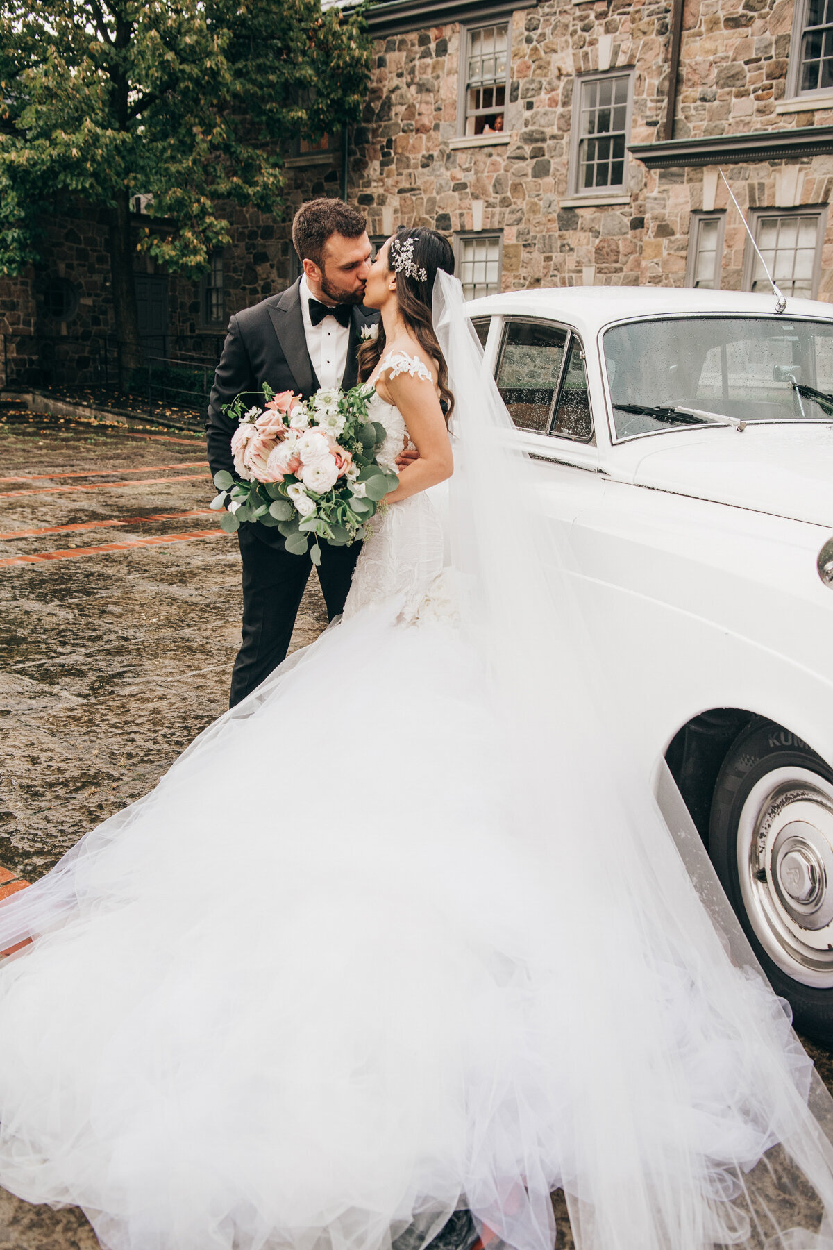 Bride and groom kiss in front of Rolls Royce getaway car