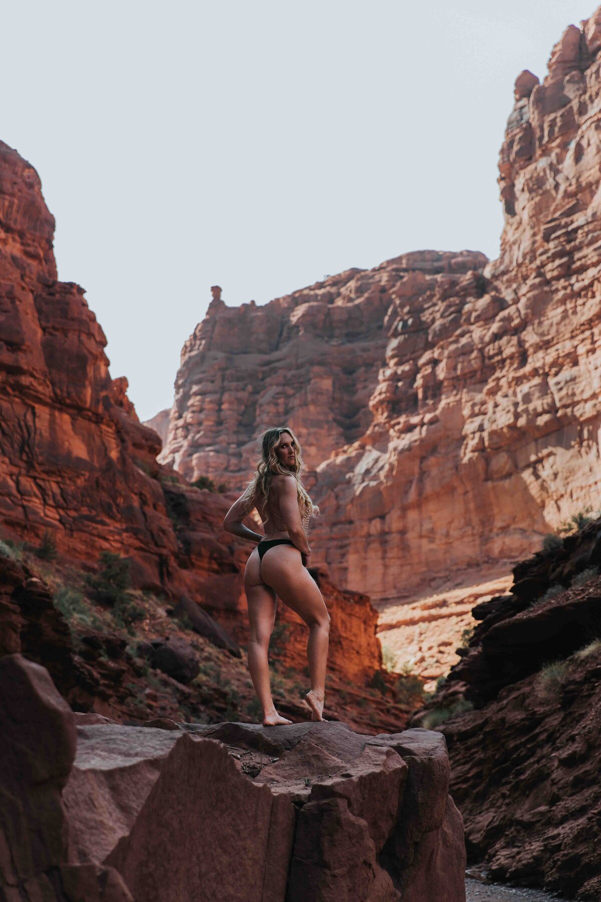 A woman is standing on a huge rock in a canyon in Moab utah