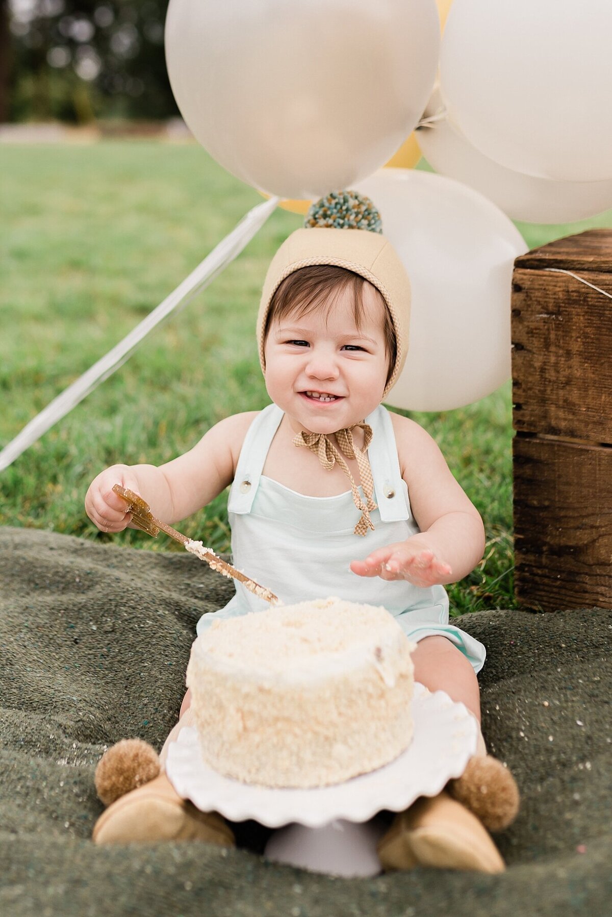 baby boy smiling with cake with hat on with pom pom for hillsboro milestone session