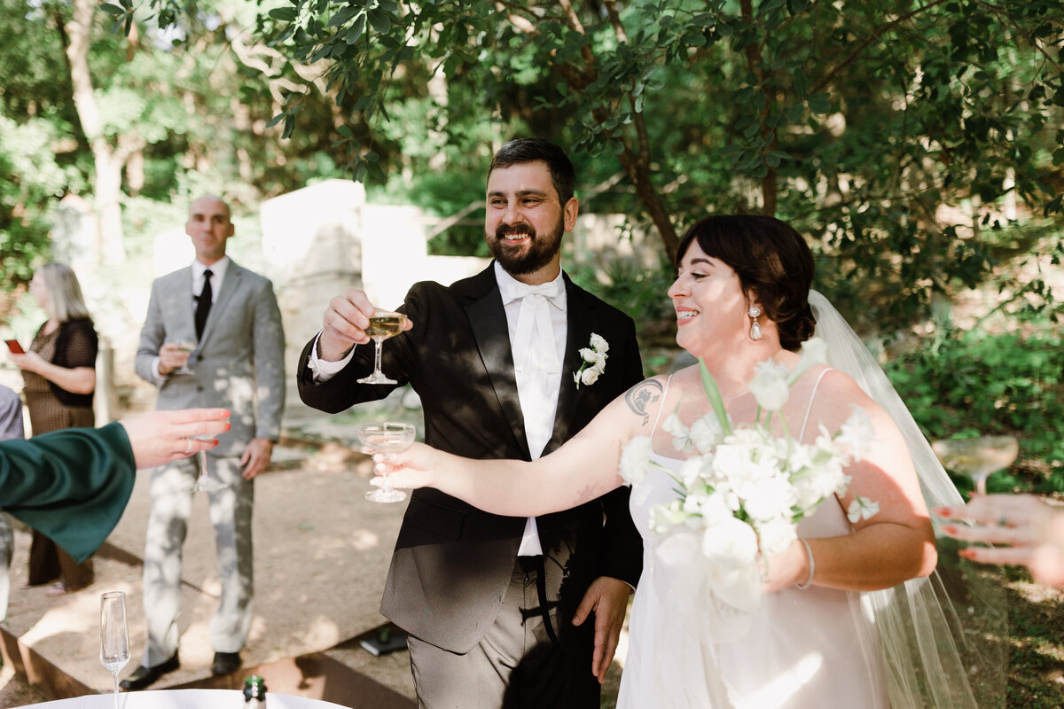 Bride and groom raising glasses at Umlauf Sculpture Garden, Austin