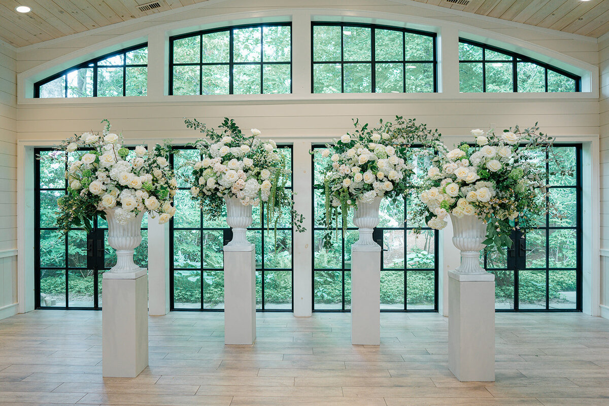 Four large white floral urns with white wedding arrangements at in indoor ceremony in Highlands, NC. 